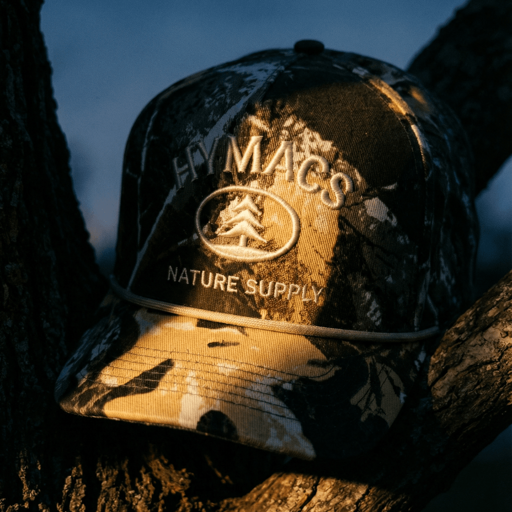 Camouflage cap with 'Macs Nature Supply' logo on a tree branch at night.