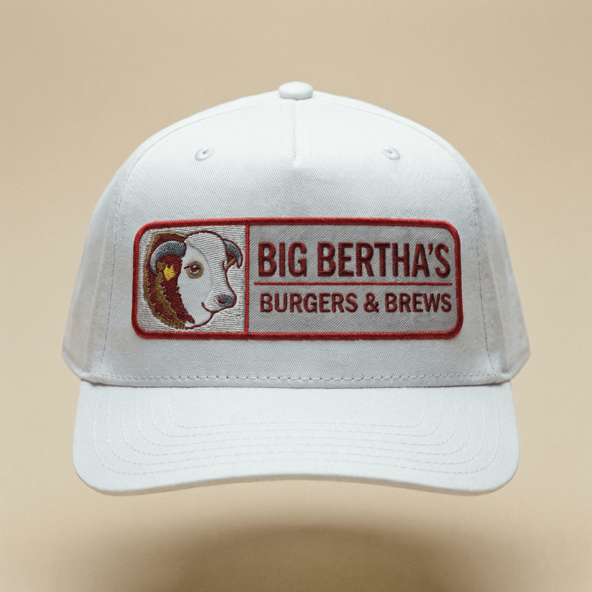White cap with 'Big Bertha's Burgers & Brews' logo on a beige background