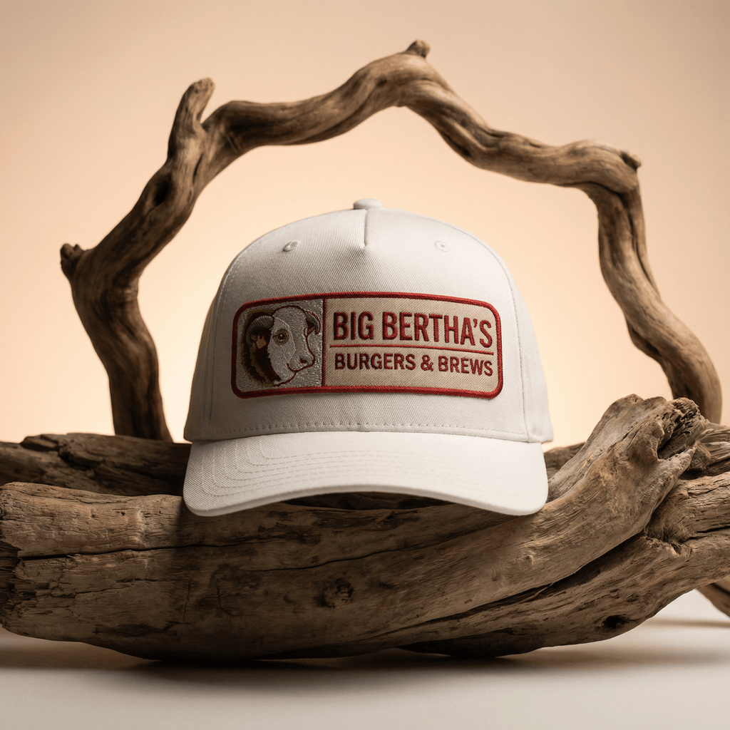 White cap with 'Big Bertha's Burgers & Brews' logo on a wooden background