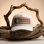 White cap with 'Big Bertha's Burgers & Brews' logo on a wooden background