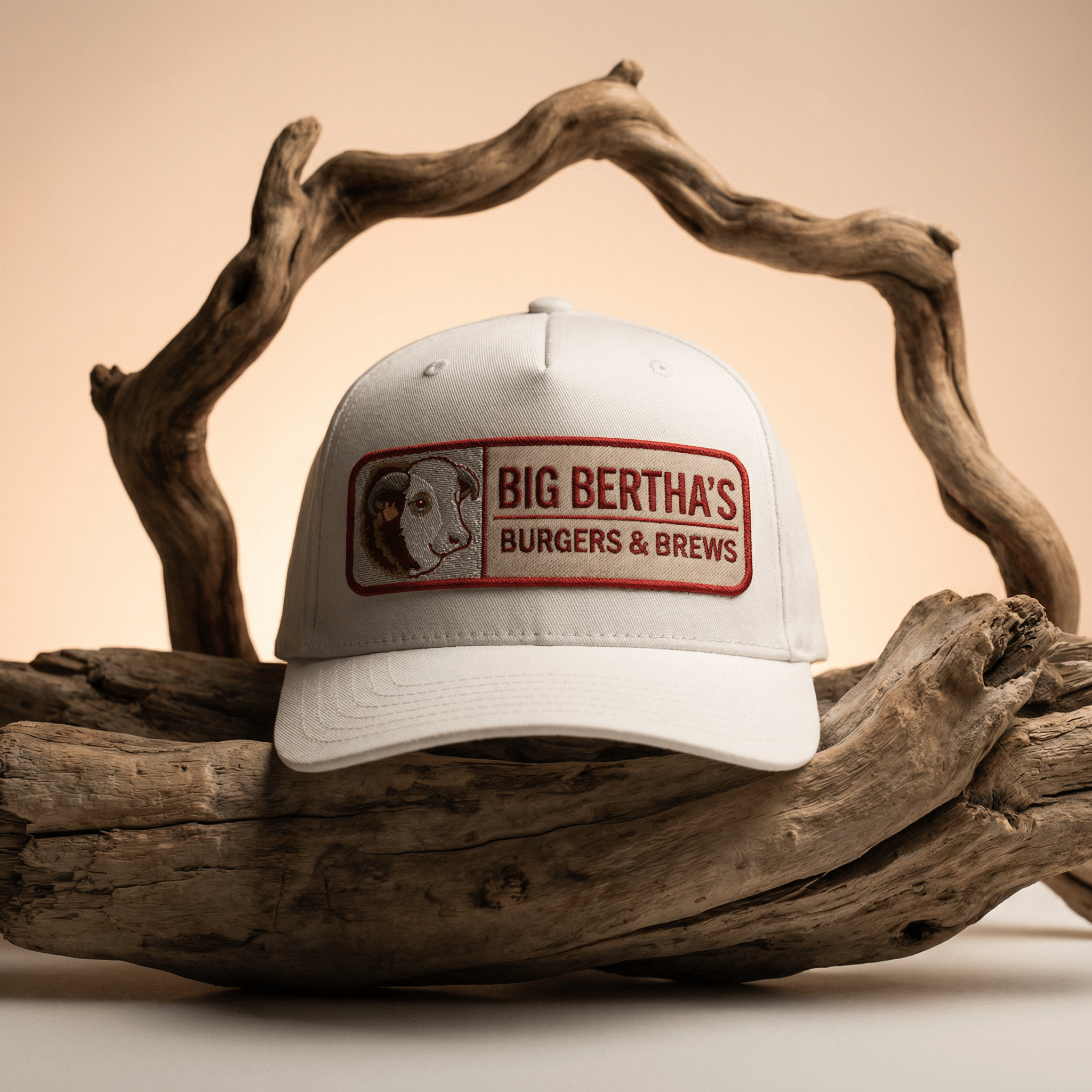 White cap with 'Big Bertha's Burgers & Brews' logo on a wooden background