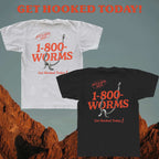 White and black t-shirts with '1-800-WORMS' text and fishing hook design on a desert background.