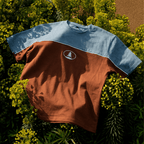 Brown and blue t-shirt with a logo on a bed of green plants